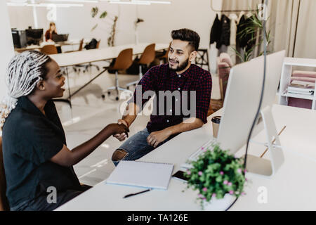 Friendly smiling indian businessman and african businesswoman handshaking over the office desk after pleasant talk and effective negotiation, good rel Stock Photo