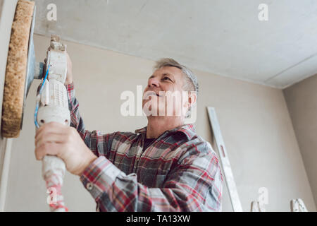 Plasterer smoothing interior wall with machine Stock Photo