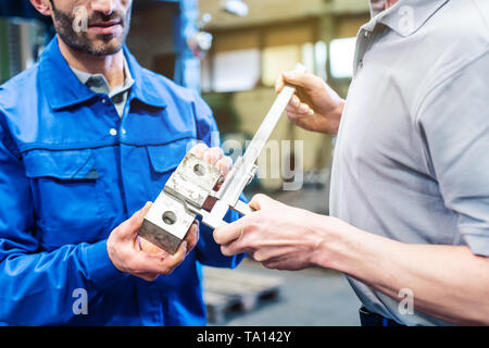 Two workers checking measurements of work piece in the factory Stock Photo