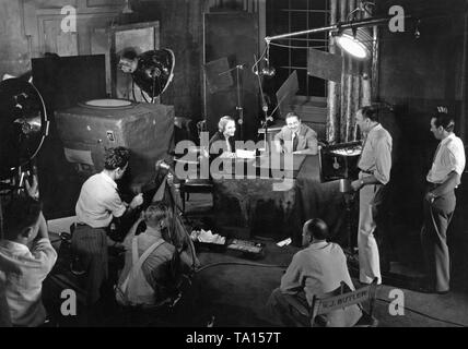 This photo was taken during the shooting of the crime film 'Attorney for the Defense', directed by Irving Cummings, at Columbia Studios in Hollywood. In the picture: Constance Cummings (sitting) and Edmund Lowe, standing beside: Irving Cummings. This movie was filmed with the best film technology of the time, the camera is hidden in a special box, the new microphone helps the actor to speak naturally. Stock Photo