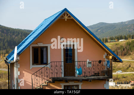 Two-storied residential cottage house top with shingle blue roof, plastered pink walls, forged balcony and outside staircase in ecological mountain ar Stock Photo