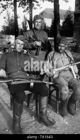 Three Russian soldiers posing for the camera in the captured Berlin. The soldier in the center and the man on the right are armed with German MP-40, a popular booty weapon among Russian soldiers. Stock Photo
