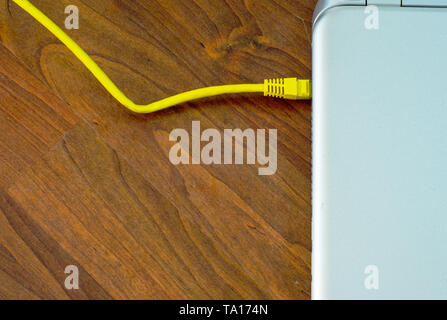 Closed laptop connected to ethernet grey cable on brown wooden floor Stock Photo