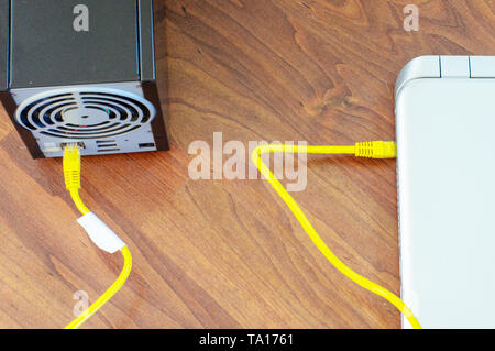 Laptop connected with NAS network device with yellow ethernet cable Stock Photo
