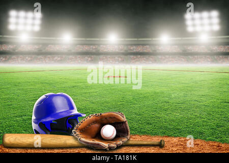 Blue baseball helmet, bat, glove and ball on field at brightly lit outdoor stadium. Focus on foreground and shallow depth of field on background and c Stock Photo