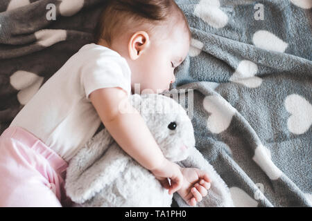 Cute baby girl sleeping with bunny toy in bed closeup. Good morning. Top view. Stock Photo