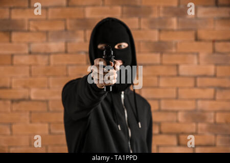 Male criminal pointing a gun at viewer against dark brick background ...