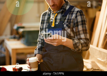Mid section portrait of modern carpenter using smartphone during coffee break in joinery, copy space Stock Photo
