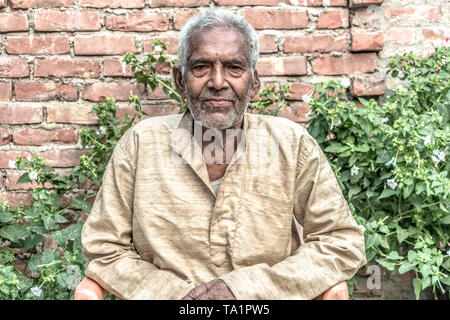 Portrait of Old aged Indian male in his 80s with white beard, wearing pale clothes, sitting relaxed in garden & leading satisfied post-retirement life Stock Photo