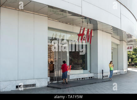 Woman entering a branch of H&M in the Old town aread of central Bucharest, Romania. A young woman is standing checking her mobile phone. Stock Photo