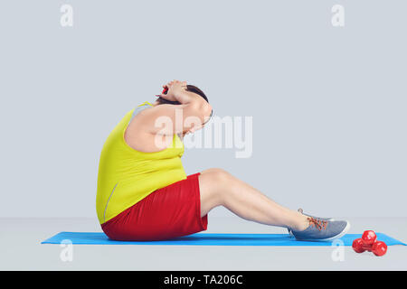 Fat funny man doing exercises on abs press on gray background Stock Photo