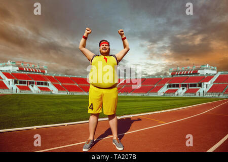 Fat man in sportswear shouts raised hands up standing in the stadium. Winner motivation concept. Stock Photo