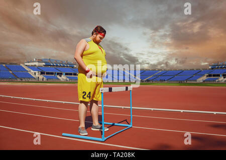 Fat man in sportswear stands in front of a barrier on a track stadium. Winner concept success obstacle problem. Stock Photo