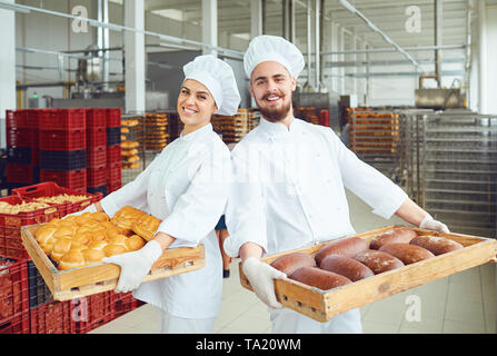 Bakers man and woman in white uniform with trays of fresh bread standing in a bakery Stock Photo