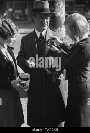 The NS-Volkswohlfahrt collects charity for the 'Hilfswerk Mutter und Kind'. A helper of the NSV pins a silk picture onto the donor's coat. Stock Photo