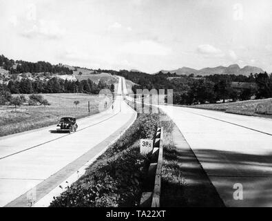 An Opel Olympia followed by a motorcyclist on the Reichsautobahn Munich-Salzburg (A 8) at Irschenberg (Km. 38.5). In the background, the Wendelstein. Stock Photo