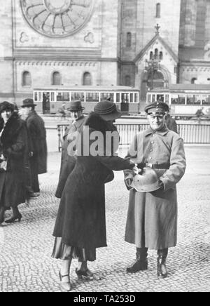 A uniformed Stahlhelm member with a matching helmet and collecting box collects donations from passers-by in front of the Kaiser Wilhelm Memorial Church on the corner of Tauentzienstrasse and Rankestrasse. Stock Photo