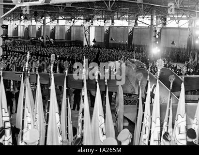 Rudolf Hess holds a speech at a conference of the Reich Chamber of Labor in the factory of Messerschmitt AG Haunstetten / Augsburg, and names the companies honored by Hitler, to which they awarded the title of 'National Socialist Model of Industry'. In the foreground, flags of the German Labor Front (DAF). Behind the lectern, a Messerschmitt Bf 110. Stock Photo