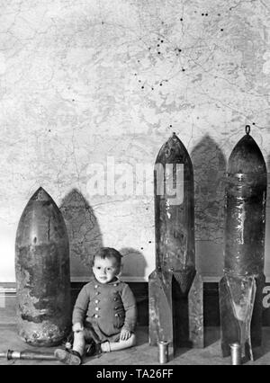 Photo of German or Italian duds in Madrid in 1937. A toddler was placed next to the aerial bombs. In the background, a map of Spain with the capital city Madrid, where the bombardments of the Spanish national troops are indicated. In front of the bombs, the detonators. Stock Photo
