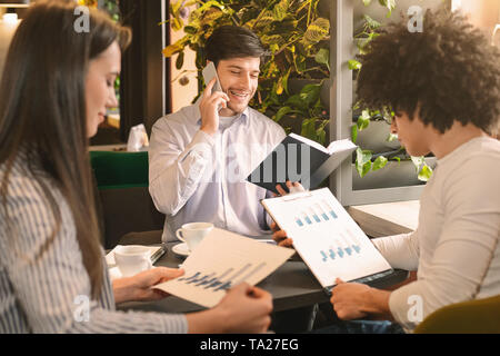 Young man calling to clients, his colleagues studying financial statistics Stock Photo
