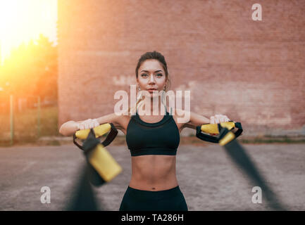 Female athlete training fitness workout in summer city. Rubber loop strap, push-up wiring hands. Active lifestyle, sportswear leggings top. Emotions Stock Photo