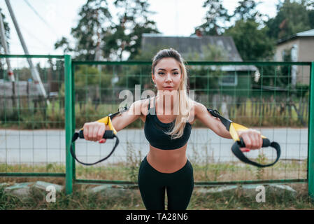 Female girl athlete training fitness workout in summer city. Rubber loop strap, push-up wiring hands. Active lifestyle, sportswear leggings top Stock Photo