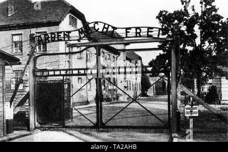 The main entrance to the Auschwitz-Birkenau concentration camp with the slogan 'Arbeit Macht Frei' (Work makes you free). The small sign saying 'Caution, high voltage, danger to life' refers to the outer barrier line secured with electric barbed wire. Stock Photo