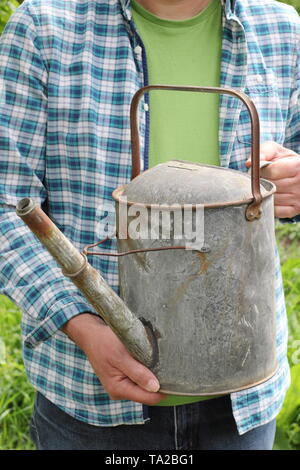 Man prepares to water garden from a metal watering can in late spring - UK Stock Photo