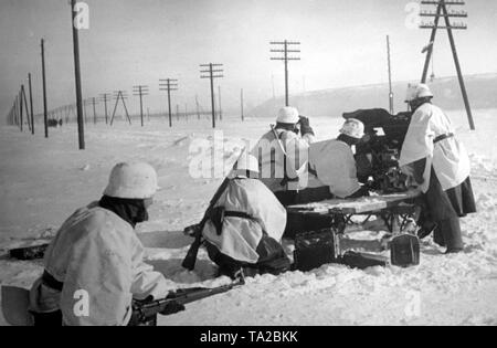 German soldiers are positioning a 3,7cm Pak 35/36 anti-tank gun on a snow-covered field west of Moscow. The soldiers still wear their summer uniforms and camouflage themselves with white bed covers and tablecloths. In the background are more soldiers marching down the street. (PK photo: war correspondent Langl). Stock Photo