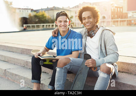 Diverse teen friends sitting outdoors with skates Stock Photo
