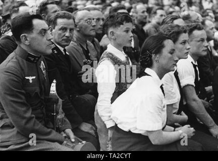 Adolf Hitler gives a speech in the Weitzer Maschinenhalle in Graz. After the annexation of Austria to the German Reich, the National Socialist dictator visited Austrian cities. On the left, a soldier who already wears the German national emblem, the eagle with the swastika, on his Austrian uniform. Stock Photo