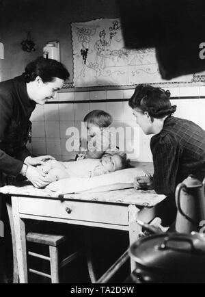 A helper of the 'Hilfswerk Mutter und Kind' of the NS-Volkswohlfahrt visits a young mother, and gives her advice on baby care in a kitchen. Stock Photo