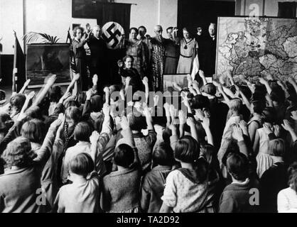 In a elementary school classroom, decorated with world war propaganda posters, a swastika flag and a map with the territories separated due to the Treaty of Versailles, teachers and students honor a 'national celebration' with singing the German national anthem and the Horst Wessel Lied (song), as well as the Hitler salute. Stock Photo