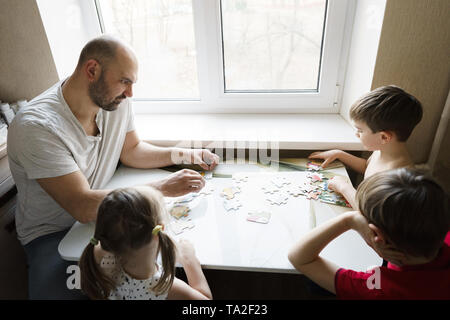 Family leisure: father, sons and daughter play board games together Stock Photo