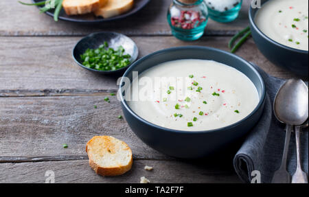 Cauliflower and potato cream soup with green onion in a bowl on grey wooden background. Copy space. Stock Photo