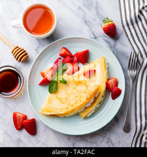 Crepes, thin pancakes with cream cheese, ricotta and fresh strawberries. Marble background. Top view. Stock Photo