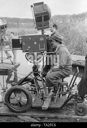 Photo of a cameraman shooting the film 'The Gypsy Baron', directed by Karl Hartl. The cameraman sits on a four-wheeled vehicle operated on rails. The camera itself is also mounted on this vehicle by means of a tripod, so both are mobile. Stock Photo