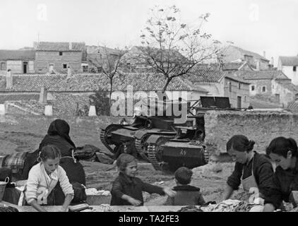 Two Soviet T-26 tanks captured by national Spanish troops. In the foreground, women and children wash clothes. Stock Photo