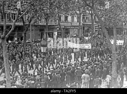 Photo of a Republican demonstration in remembrance of the 19. anniversary of the October Revolution (November 1917) on the Rambla (Promenade Las Ramblas) at the beginning of November, 1936. The marching military policemen carry a banner: 'The military police (Carabineros) greet their Soviet-Russian brothers.' The police officers in uniform raise their fists saluting. Passers-by watch the scene on the pavement. Stock Photo