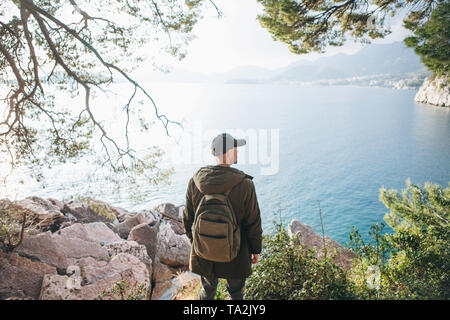 Tourist with a backpack near the sea. Travel alone. Looks into the distance. Stock Photo