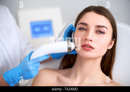 Beautician doctor doing rf-lifting procedure for flawless woman face laying on medical chair in a beauty salon. Hardware cosmetology. Patient receivin Stock Photo