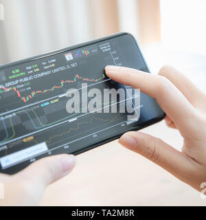 Female hand with smartphone trading stock online in coffee shop , Business concept Stock Photo