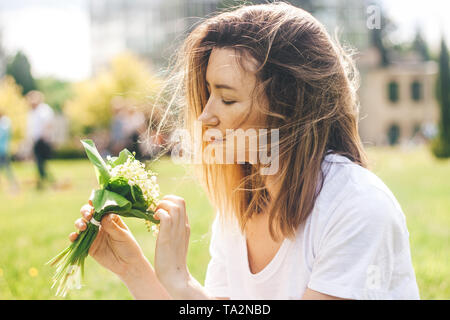 Woman holding lovely bouquet of of lilly of valley flowers in the sunny warm day Stock Photo