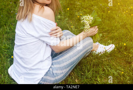 Woman sitting on the ground and holding lovely bouquet of lilly of valley flowers in the park Stock Photo