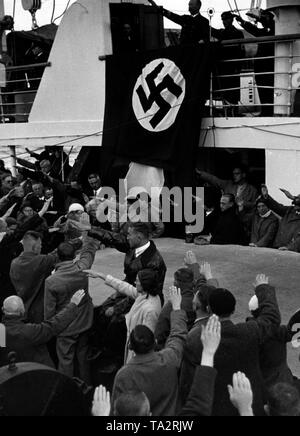 Holidaymakers of the Nazi organization 'Kraft durch Freude' show the Nazi salute aboard a Kdf-ship. Above a swastika flag a ship officer. Stock Photo