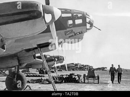 Photo of German Heinkel He 111 fighter bombers of the Condor Legion (combat group 88) on the airfield of Lerida, Catalonia, 1939. In front of the bombers there are grenades. Two officers of the ground personnel are walking beside them. Pictured, the forward gunner compartment, which was made of plexiglass with an integrated machine gun for the defense from fighter aircrafts. Stock Photo