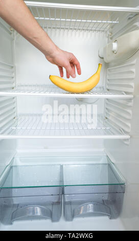 A man's hand reaches out for a single banana in an open, empty refrigerator. Weight loss diet concept. Stock Photo