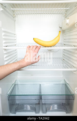 A man's hand reaches out for a single banana in an open, empty refrigerator. Weight loss diet concept. Stock Photo