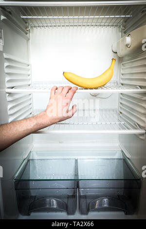 A man's hand reaches out for a single banana in an open, empty refrigerator. Weight loss diet concept. Stock Photo
