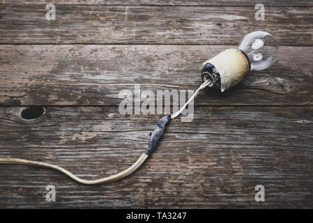 Retro lightbulb with damaged wires, vintage wooden background with space for text. Concept - neglect of fire safety. Stock Photo